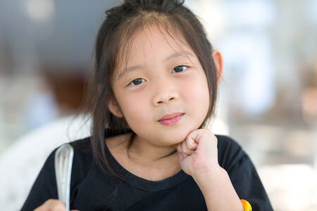 Portrait of Cute Asian Child at Restaurant Holding Spoonの写真素材