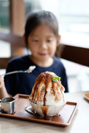 Happy Asian child enjoys eating Korean Patbingsu or Bingsu, shave ice frozen dessert.の写真素材