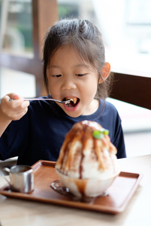 Happy Asian kid enjoys eating shave ice frozen dessert.の写真素材