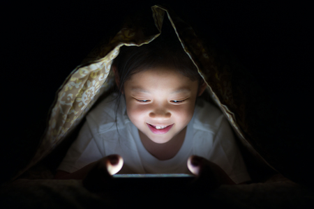 Asian Child Using Tablet PC in Bed at Nightの写真素材