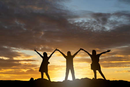 silhouette Three young people standing with hands on the sunset backgroundの写真素材