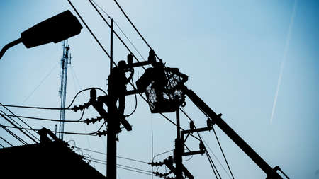 Silhouette workers installing electrical equipment on utility poles.