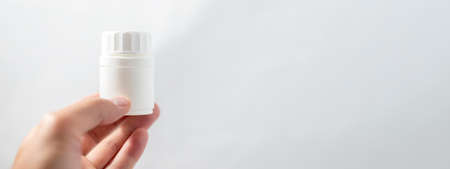 White medicine plastic package or jar for pills in male hand on white background. copy space, banner, medical conceptの写真素材