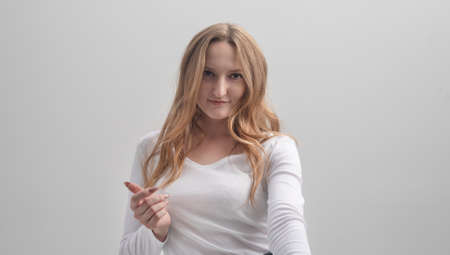 Portrait of female woman, winking flirty at camera and smiling joyfully, beckoning with index finger over gray background, studio shotの写真素材