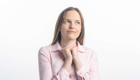 Happy praising joyful caucasian woman with arms holding together looking up and praying on white background in studio.の写真素材