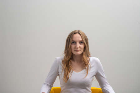 Studio portrait of serious focused caucasian young woman wearing white T-shirt, looking calmly and...