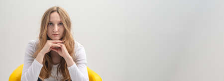 Portrait of a thoughtful pensive young caucasian woman thinking while sitting in yellow chair,...