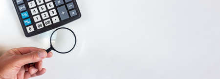magnifying glass and calculator on white table, banner, copy space, male handの写真素材