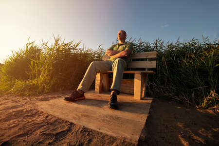 Relaxed man outdoor. man relaxing on long chair on nature in sunset rays of sun, senior adult mature man, bottom viewの写真素材
