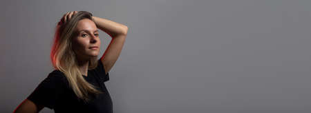 Pretty young arrogant woman in black t-shirt posing over dark background with hand over head, red light, copy space, bannerの写真素材