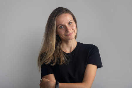 Beautiful young smiling friendly and confident woman portrait looking at camera calmly with crossed arms. Studio shot, isolated on gray backgroundの写真素材