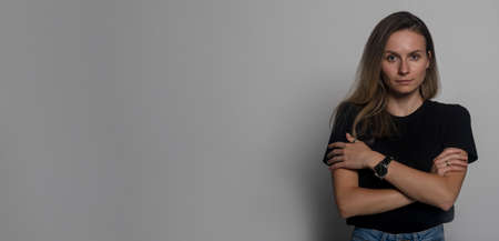 Offended girl looks at camera pose over gray studio background self hug closed pose folded crossed arms on chest, woman feels lonely cheated suffering from bullying or abuse, copy space, bannerの写真素材