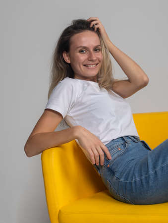 Attractive happy young woman relaxing on chair smiling and looking at camera, studio shotの写真素材