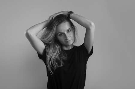 calm friendly girl with hands by her head looking at camera over gray background, black and white or gray colors photoの写真素材