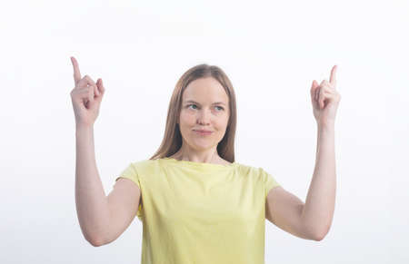 Young woman wearing yellow top standing isolated on white background pointing up at copy space for...