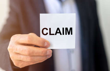 Businessman holding a paper card with text Claim in hand, lawsuit and claim concept