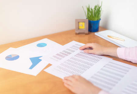 accountant or banker making calculations sitting at office table with documents with tables on desk pointing at digits on documents. Savings, finances and economy concept, working with documentsの写真素材