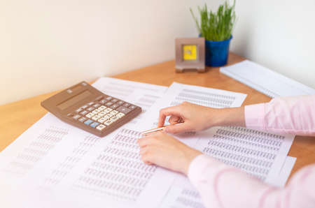 accountant or banker making calculations sitting at office table with documents with tables on desk pointing at digits on documents. Savings, finances and economy concept, working with documentsの写真素材