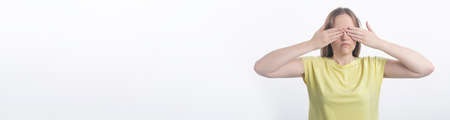 young woman closing her eyes with both hands over white background, studio, copy space, bannerの写真素材