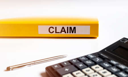 Claim word on folder on office table, claim or lawsuit concept, white table with calculatorの写真素材
