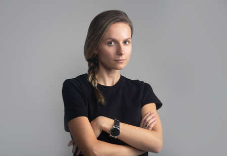 Studio head and shoulders portrait on gray of a beautiful serious young woman looking directly at the camera, black t-shirtの写真素材