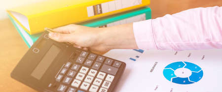 female accountant or banker making calculations sitting at office table with documents with tables...