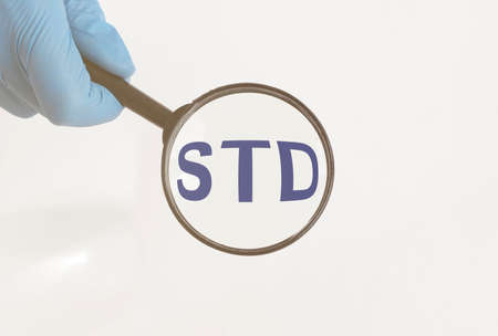 word STD through magnifying glass lens in protective doctor gloves. Medical concept. doctorの写真素材