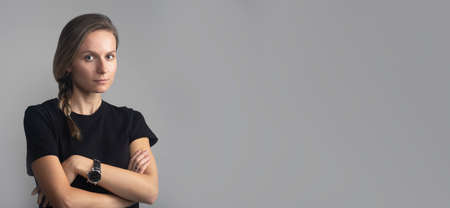 Studio head and shoulders portrait on gray of a beautiful serious young woman looking directly at the camera, black t-shirt, copy space, bannerの写真素材