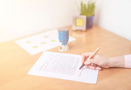 Businesswoman is signing a contract at office table with folders, stamp and contract, signing agreement close upの写真素材