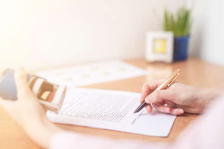 Businesswoman is signing a contract at office table with folders, stamp and contract, signing agreement close upの写真素材