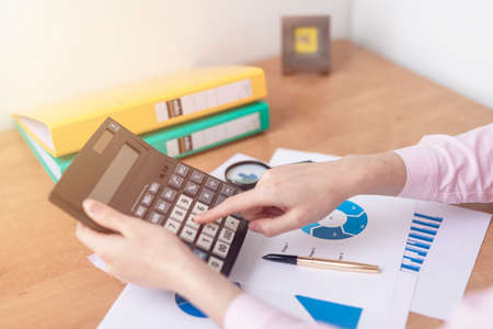 female accountant or banker making calculations sitting at office table with documents with tables...