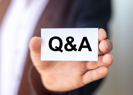Q and A - Questions and Answers text on business white card close up in hands of businessman.