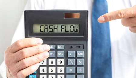 CASH FLOW word text inscription on calculator in a male hand of a businessman in white shirt and...