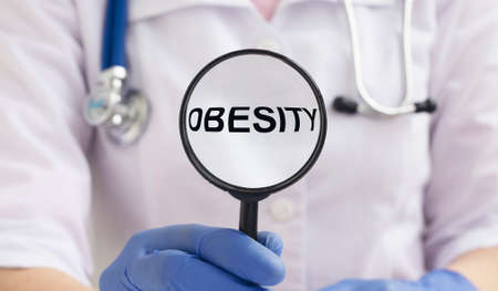Obesity Word through magnifying glass in hands of doctor, medical concept.の写真素材