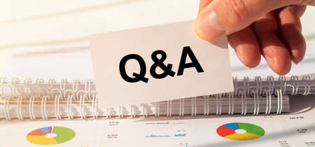 Q and A - Questions and Answers text sign on business white card over office table in male hand,...