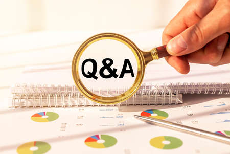 Q and A - Questions and Answers text sign on through magnifying glass over office table in male...