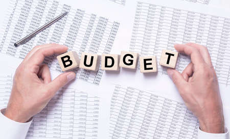 Budget the word on wooden cubes in male hands on financial documents with digits, accounting conceptの写真素材