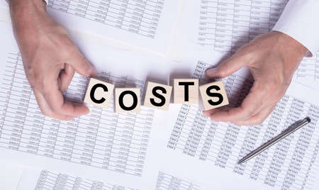 costs word on wooden cube blocks on financial documents, top view.の写真素材
