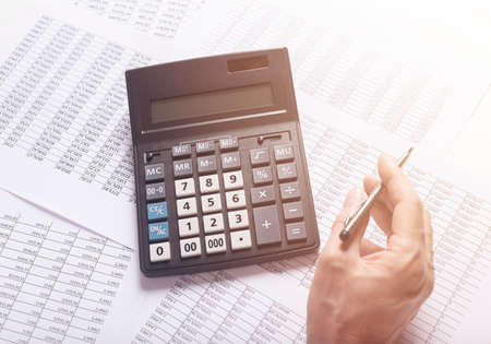 financial analysis concept, male hand with pen using a calculator over accounting documents.