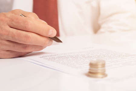 Contract signing concept. Businessman with pen over document closeup. money coins on foreground...