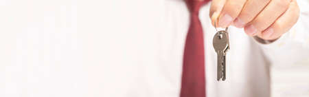 businessman realtor offering keys to camera sitting at office table in shirt and red tie. banner, copy spaceの写真素材