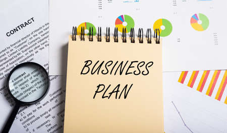 Business Plan inscription on yellow spiral notebook on office table with documents charts contract and loupe, top view, bannerの写真素材