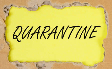 word QUARANTINE on yellow table through torn craft paper, flatly, top view.の写真素材