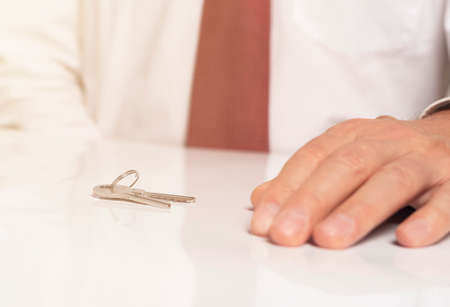keys on white glossy table with close-up hand of businessman in tie.