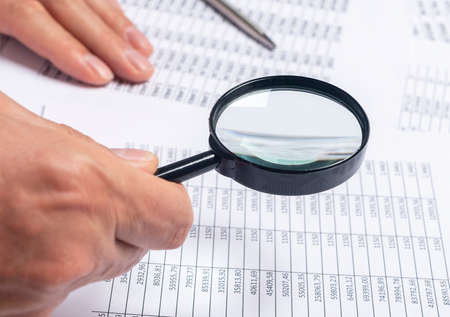 financial documents with magnifying glass over them in male hands, business research concept.