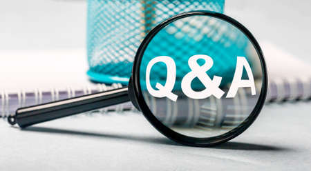 magnifier with text Q and A and business documents on table close up