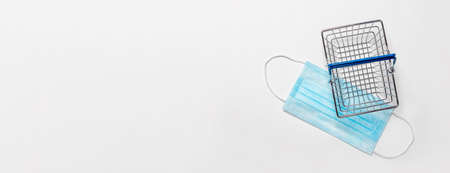 Metal empty shopping basket over white background with medical facial mask, top view.