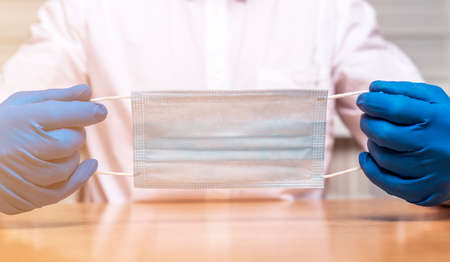 Protective facial medical masl closeup in hands in gloves of a male doctor.の写真素材