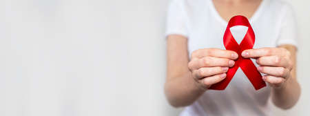 Red ribbon for aids and hiv world day support, close up. Advertizing horizontal banner with copy space for text. Blurred woman in white on background.の写真素材
