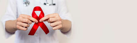 Red ribbon for aids and hiv world day support, close up. Hand of female doctor. Horizontal banner...